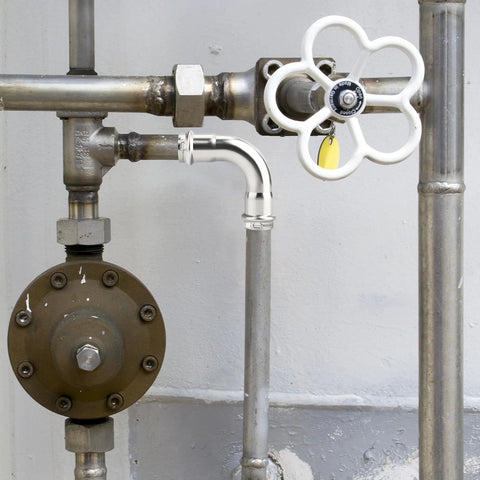 1‑inch stainless steel press slip 90° elbow installed in a residential plumbing line with a white valve handle nearby
