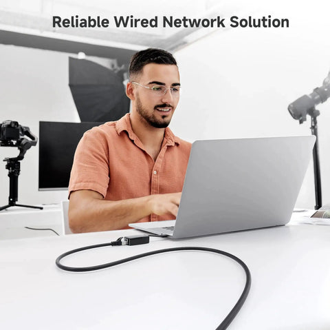 Man using laptop with 10 Gbps Snagless Shielded Cat6A Ethernet Cable 50ft Black for fast gig speed LAN networking on a desk.