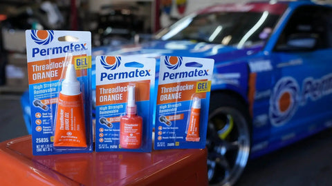 Permatex Orange Threadlocker tubes and packaging in front of a sports car, designed for high vibration machinery removable with hand tools.
