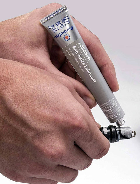 Person applying Anti Seize Lubricant 81343 1 Oz Tube Four Pack With Aluminum Copper And Graphite Blend Salt And Moisture Resistant Marine Grade Formula For No Fuss Spark Plug Removal, Cylinder Head Bolts, And Quick Disassembly to a spark plug.