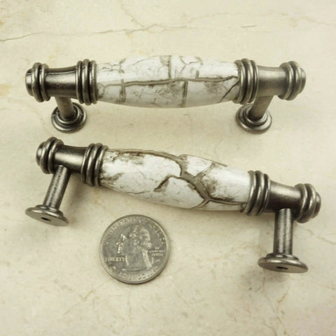 Two decorative cabinet pulls with marble-look design and silver hardware next to a quarter for scale.
