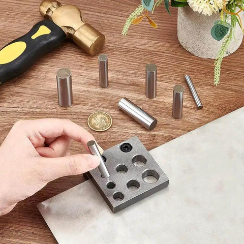 Hand using Heavy Duty Carbon Steel Disc Cutter Set for jewelry making with six cutting punches seen on a wooden table.