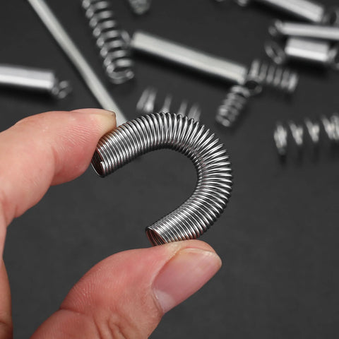 Compression spring close-up, curved zinc-plated steel wire held between fingers.