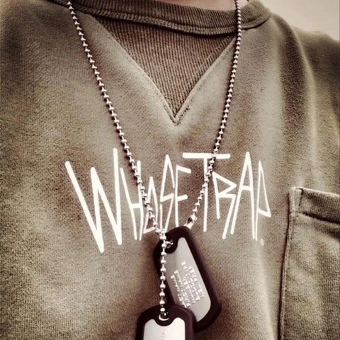 Person wearing a ball chain with dog tags, with "WHASETRAP" printed on the shirt.