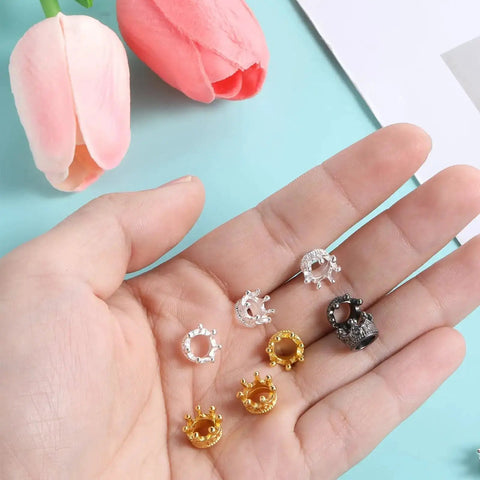 Hand holding gold, silver, black crown charms from Mini Crown Beads 60 Pcs Set for DIY Jewelry Making Gold Silver Black 3D Alloy Crown Charms