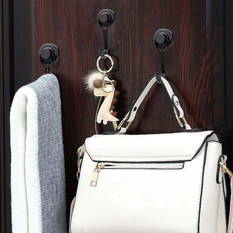 Coat and bag hanging on black hooks attached to a dark wooden surface, with a dinosaur keychain on the bag.