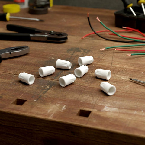 Nine white ceramic wire nuts for high-temp electrical connections on a wooden workbench with pliers and wires nearby