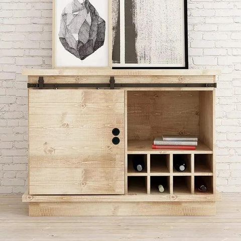 Light wood cabinet with sliding door and black handles, wine storage, and decorative art pieces on top against brick wall backdrop.