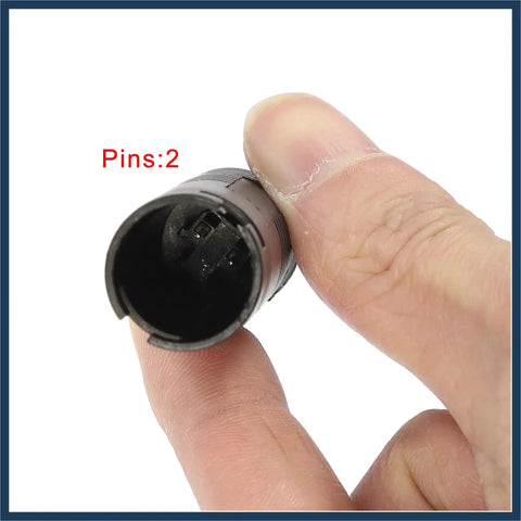 Close-up of a two-pin car brake pad wear sensor, black plastic, held between fingers