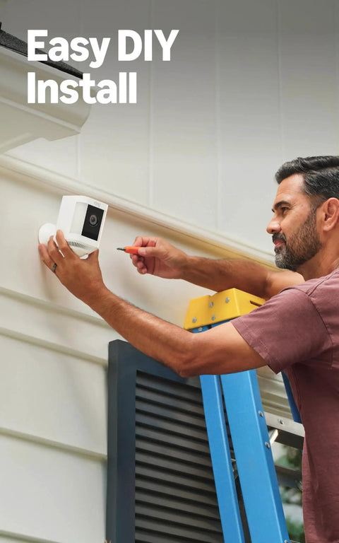 Man installing Spotlight Cam Plus Battery Security Camera With HD Video Color Night Vision on house exterior.