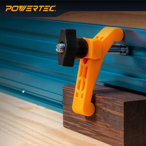 Two Pack Mini Hold Down Clamps For T Track Systems Three And A Quarter Inch Long By Three Quarters Inch Wide Includes Two And A Half Inch T Track Bolts Thumb Knobs And Swivels Ideal For CNC Machines Table Saw Sleds Drill Presses And Workbenches, installed on a blue T-track, clamping a wooden piece with an orange plastic body and black knob.