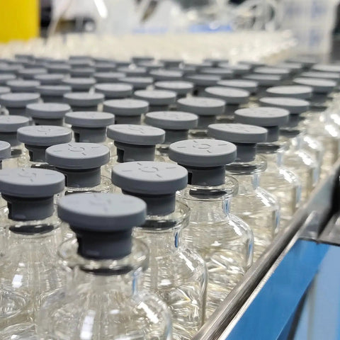Close-up of glass vials with gray rubber stoppers on a production line, focused on uniformity and sealing quality