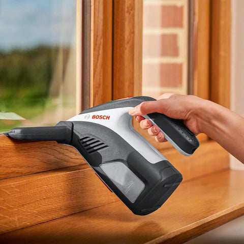 Bosch GlassVAC battery window vacuum cleaner, handheld gray/black with Bosch logo, cleaning a wooden window frame.
