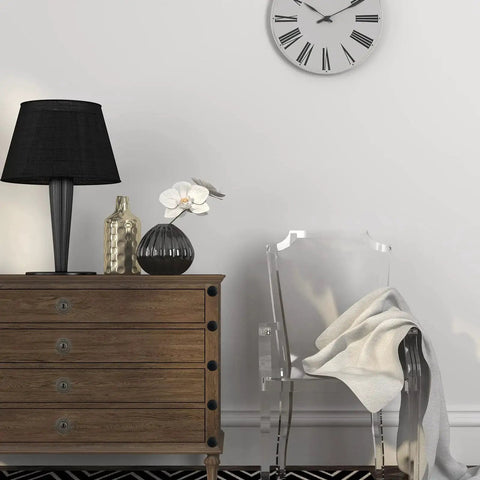 Modern living room with wood dresser, black lamp, decorative vases, transparent chair, and wall clock in simple interior design.