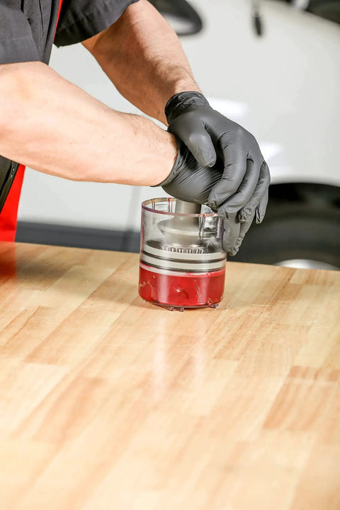 Hands using Two Piece Deluxe And Standard Bearing Packer Kit for quick flushing and repacking of wheel bearings on a wooden table.