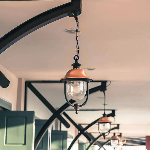 Outdoor pendant lamp hanging with chain from ceiling, featuring vintage style with glass shade under a covered patio.