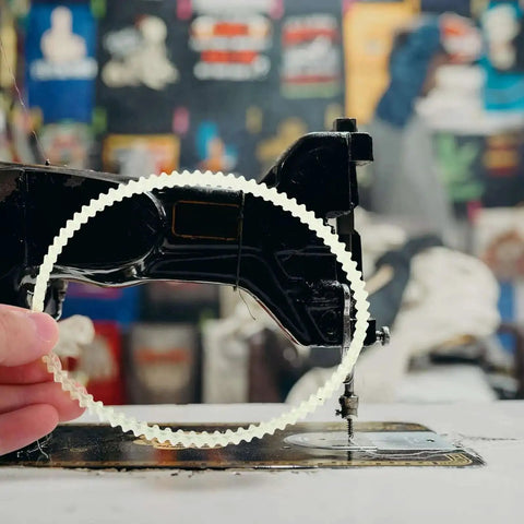 Person holding a rubber drive belt in front of a vintage sewing machine. Beef Up Your Sewing Setup With This 20 Pack Rubber Drive Belts For Sewing Machine Motors Replacement Parts For Household And Industrial Sewing Machines Pedal And Treadle Use Precise Fit Stable Transmission Quiet Operation.