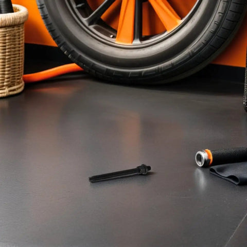 Garage floor with orange accents showing a black Crankshaft Belt Removal And Pulley Puller Tool Kit For Vehicle Engine Repair With Gear Bearing Puller And Drive Pulley And Timing Gear Compatibility Pro Grade Heavy Duty Auto Repair Set For Fast Easy Engine Fixes placed on the ground near a car wheel.