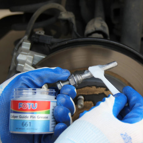 Brake caliper guide pin grease jar labeled FOTU 661 being applied with blue gloves near the brake rotor.