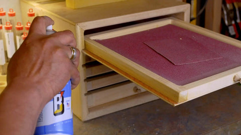 Applying 16 TDL Advanced Dry Lube With Teflon to a wooden drawer with sandpaper in workshop settings.