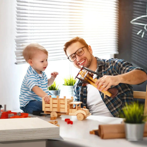Father and son playing with wooden models at a table in a bright room, surrounded by plants and natural light.