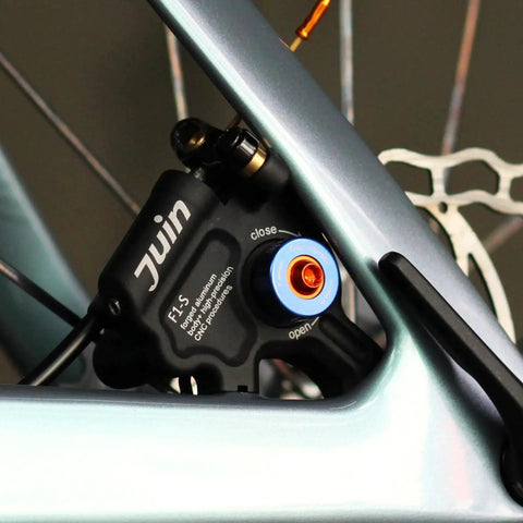 Juin F1-S black hydraulic disc brake caliper mounted on bicycle frame with blue adjustment knob