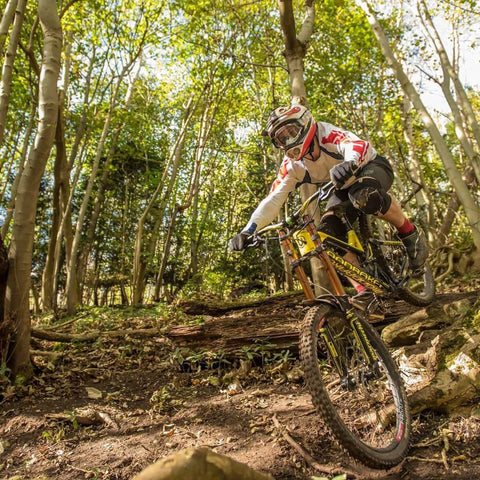 Mountain biker navigating trail in wooded area with dappled sunlight filtering through trees.