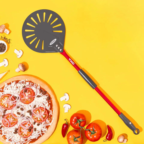 Pro Grade 9 Inch Perforated Pizza Peel With Extendable 27 To 41 Inch Handle For Indoor And Outdoor Ovens, Lightweight Aluminum Turning Peel, Nonstick Metal Pizza Turner Red TKC next to pizza and fresh ingredients
