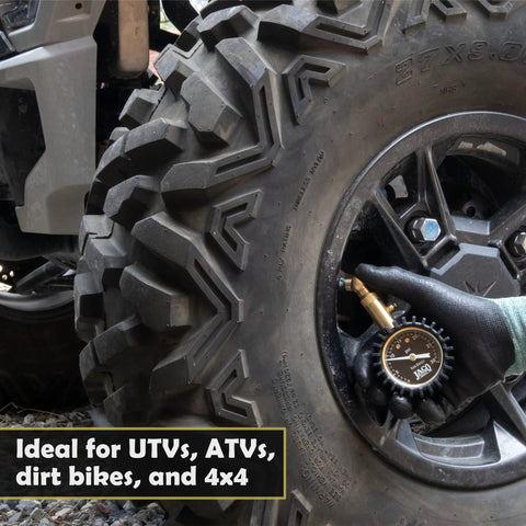 JACO Elite low-pressure tire gauge with brass nozzle, black body, used on an off-road tire by a gloved hand