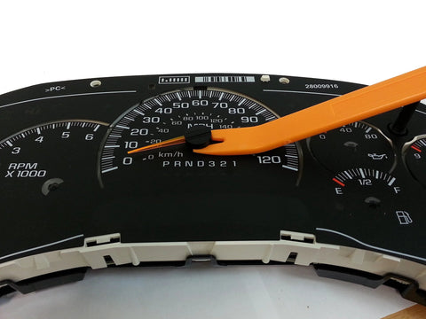 Front view of GM instrument cluster featuring speedometer and tachometer with orange plastic pry tool resting on the dial.