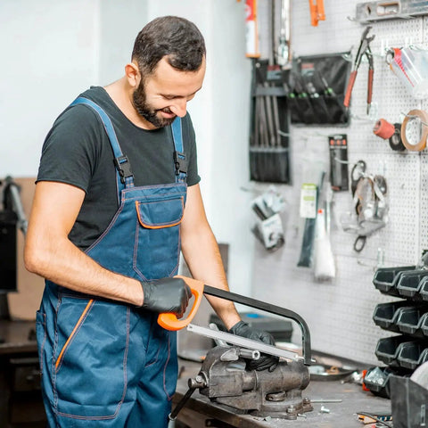 Worker cutting metal tubing with saw for machinery equipment