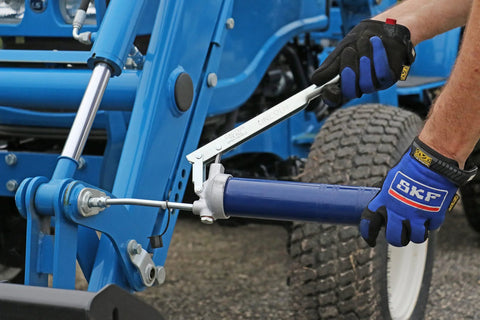 Lincoln lever-action grease gun with HD cast iron pump head on blue machinery, user wearing SKF gloves