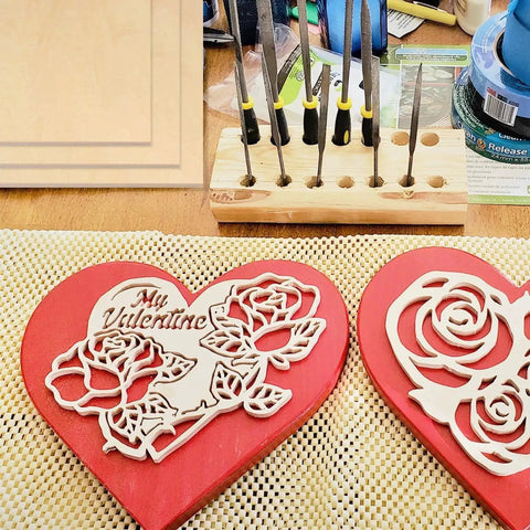 Heart-shaped wood carvings with floral designs on a crafting table near tools and supplies.