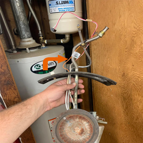 AO Smith gas water heater in a closet; hand holds curved metal heat shield with exposed thermopile wiring.