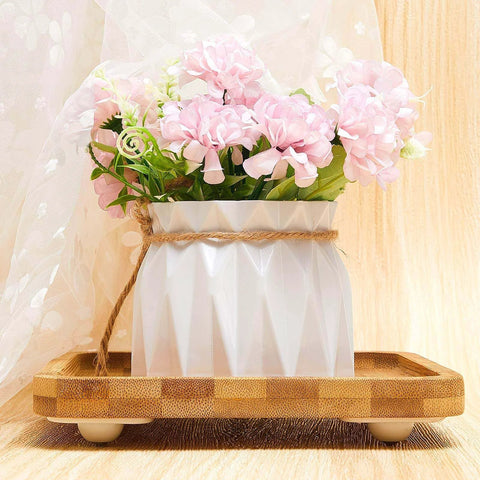 Pink flowers in white vase on wooden tray with fabric background