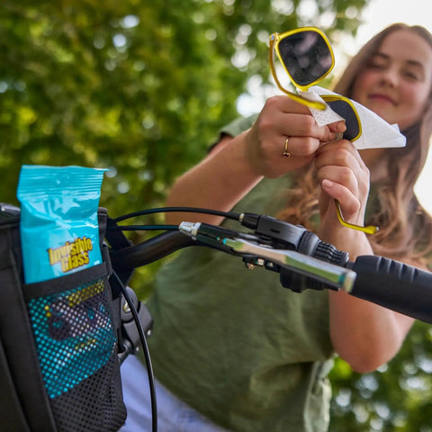 Woman using Streak Free Lens Cleaning Wipes For Glasses Cameras Binoculars 16 Count to clean sunglasses by a bicycle.