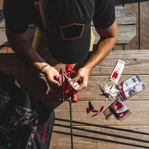 Man using Pro Class Fletching Jig for 5.5in vanes and feathers, positioned on table with tools, displaying magnetic clamp and precise offset