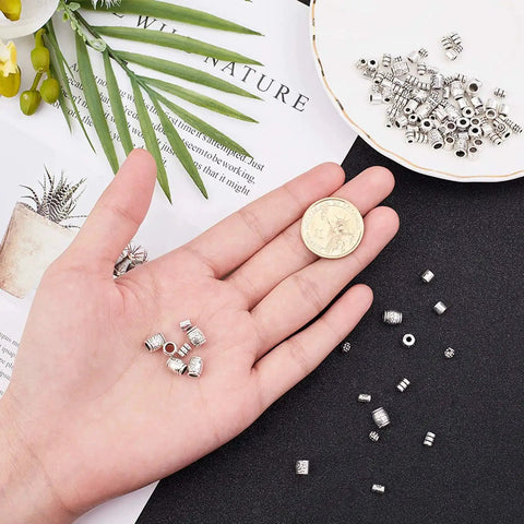 Hand holding Tibetan spacer beads from 260 Pcs Tibetan Spacer Beads Set 7 Styles Antique Silver Column Tube Metal Spacers for jewelry making.