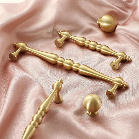 Two Pack 5 Inch Center Solid Brass Cabinet Pulls In Vintage Gold Brushed Finish on pink fabric background