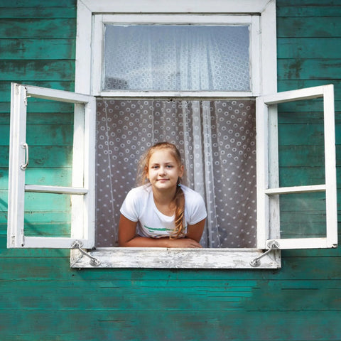 Open wooden window with double panels and a girl leaning out, showcasing a vintage latch system against a green exterior wall.