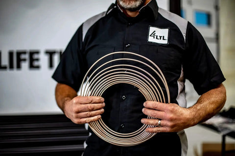 Front view: copper-nickel brake line tubing coils held by a mechanic in a black work shirt