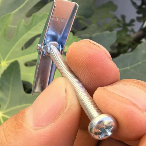 Close-up of hand holding a 1/4x3 inch carbon steel toggle bolt with spring wing, part of a pack of 50 for hollow wall surfaces.