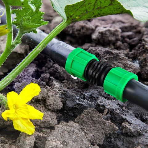 Drip irrigation coupling, 5/8 inch universal connector, green plastic fittings on black tubing in garden soil.