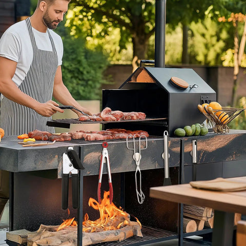 Front view of black outdoor charcoal grill with grilling tools hanging on the side rack and meat on the grates