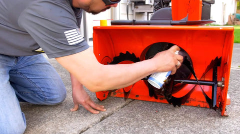 Person applying 6-16-TDL Advanced Dry Lube With Teflon 9.3 Oz Pack Of 6 to snowblower component, showcasing lubricant use on machinery.
