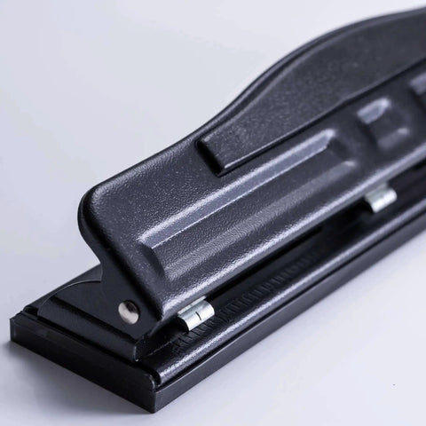 Side view of black adjustable two to three hole punch with padded handle, 11 sheet capacity for home or small office use on letter size docs.