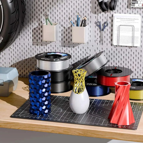 Various 3D printed vases with PETG 3D Printer Filament 1.75mm 1kg Army Green for Ender on a workshop table.