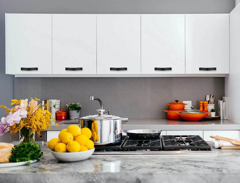 Modern kitchen with white cabinets featuring black leather drawer pulls and various colorful kitchenwares on the counter.