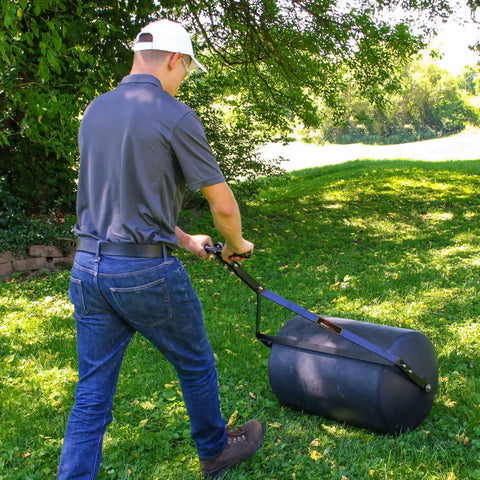 Person using powerful 270 lb poly lawn roller for push or tow with easy turn tethered plug and quick filling drum in garden