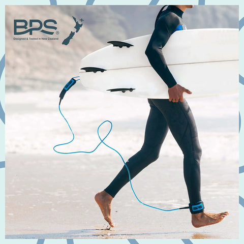 Surfer walking on beach carrying board with Storm 8mm Surfboard Leash 8 Ft Premium Leg Rope attached, Koru Dark Blue